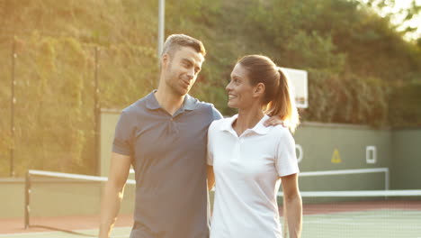 feliz pareja abrazándose y saliendo de la cancha de tenis a la luz del sol
