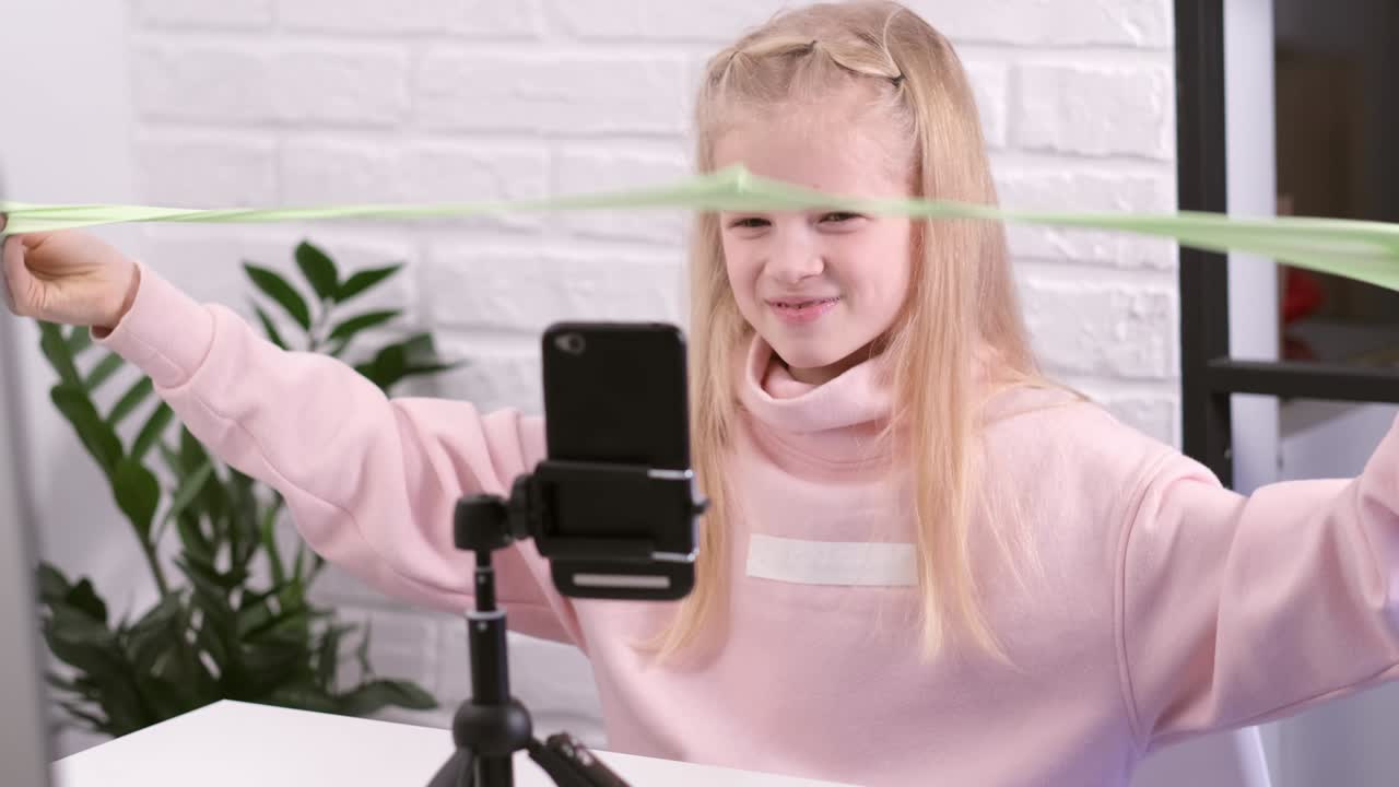 pequeña influyente blogger chica hablando con seguidores transmisión en vivo jugando con limo verde. juguete líquido de moda estirándose hacia el lado. niño mirando a la pantalla del teléfono inteligente en casa. cámara lenta
