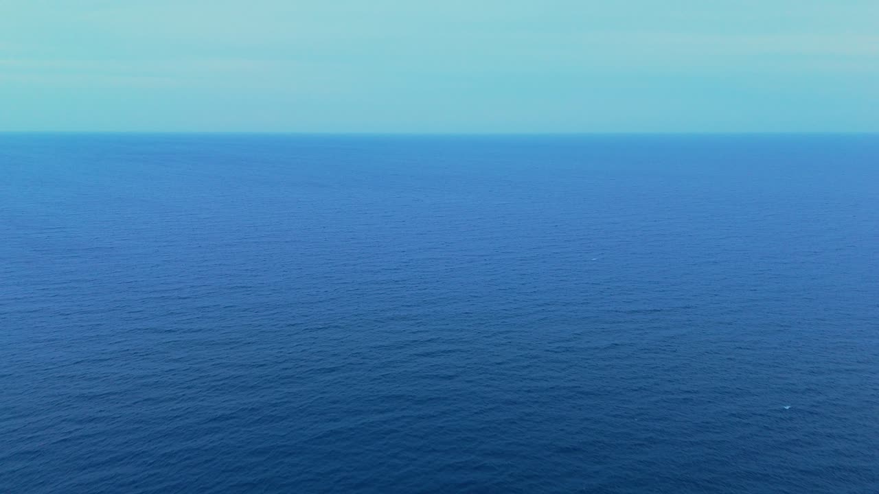 Wide aerial shot of the deep blue ocean with a gentle breeze creating subtle waves