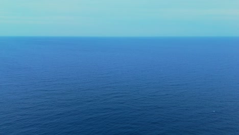 Wide aerial shot of the deep blue ocean with a gentle breeze creating subtle waves
