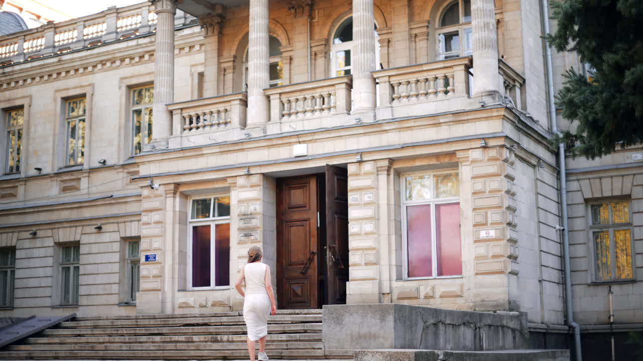 Elegant woman with flowing hair and white dress walks up the stairs of a classic architectural building