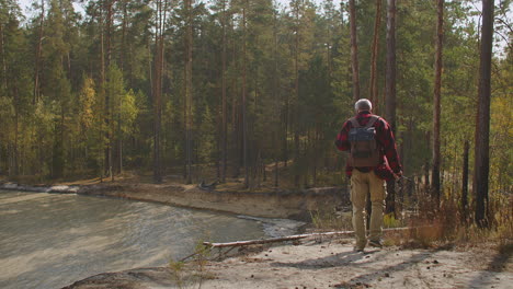 lonely middle-aged man is exploring forest with pond walking alone at fall day enjoying good weather