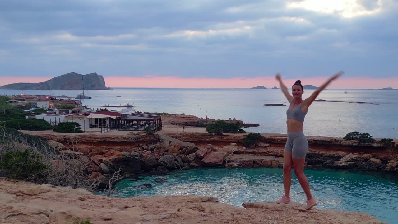 increíble vista aérea de arriba vuelo posición de chica de yoga árbol atardecer acantilado playa isla de ibiza españa drone descendente