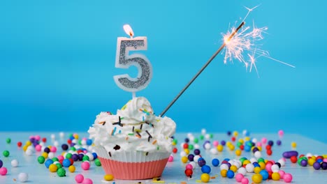 happy birthday greetings to 5 year old child, birthday cupcake with candles and birthday decorations on blue background. copy space