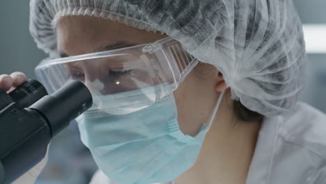 scientist in protective mask and goggles using microscope in laboratory