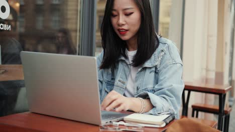 Junges-Brünettes-Attraktives-Und-Lächelndes-Mädchen,-Das-Am-Tisch-Auf-Der-Caféterrasse-Sitzt-Und-Am-Laptop-Arbeitet-Und-Dann-Eine-Brille-Aufsetzt