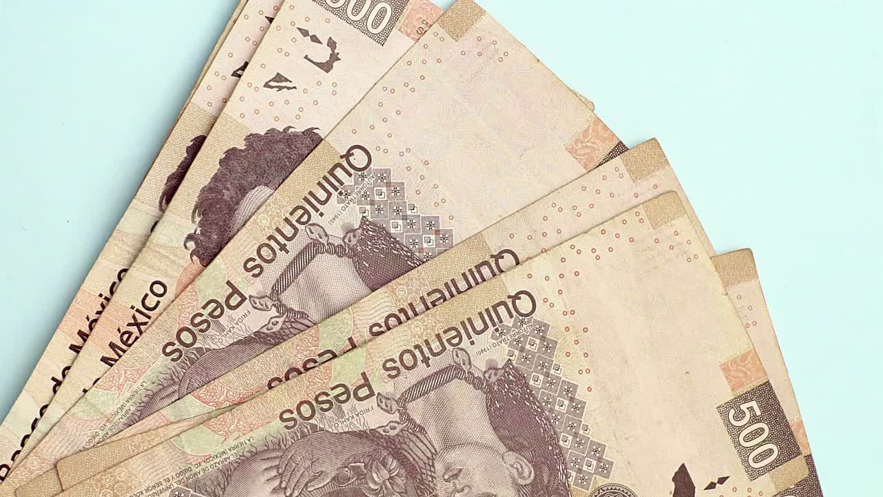 primer plano vertical de billetes de 500 pesos mexicanos colocados sobre una superficie azul