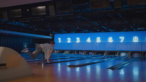 Un-Joven-En-Una-Bolera-Lanza-Una-Pelota-En-Cámara-Lenta-Y-Derriba-Bolos.-Jugar-Bolos.-Tirar-Bolas-Al-Suelo-Del-Club-De-Bolos