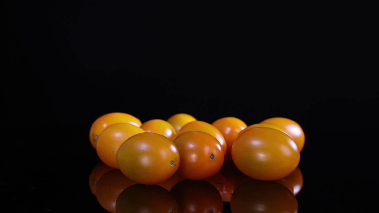 Yellow tomatoes rotate on a reflective black surface under soft lighting, creating a dynamic visual effect