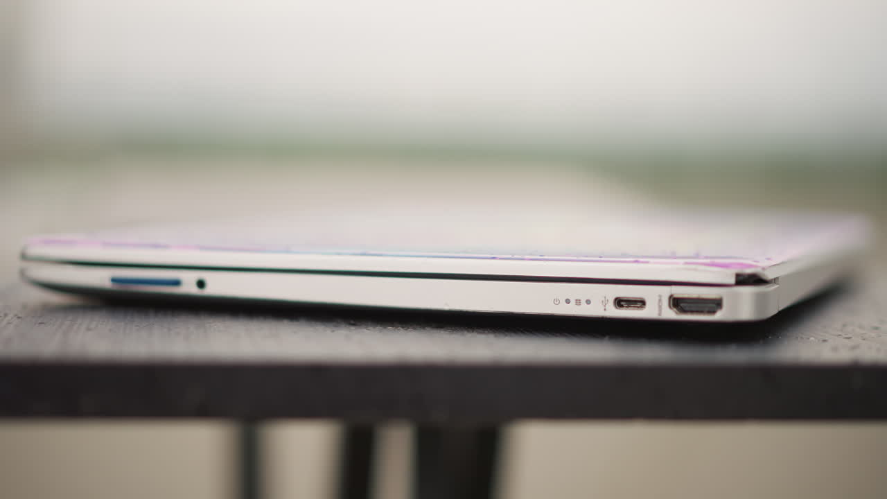 Laptop chiuso su un tavolo del caffè, profondità di campo ridotta con sfondo bokeh sfocato, sottile notebook argento che mostra le porte, appoggiato su un tavolo da bistrò in metallo, atmosfera urbana minimalista che suggerisce un DJ portatile.