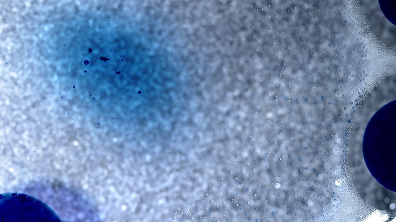 Blue ink dissolving in bubbles, creating abstract textures in macro view