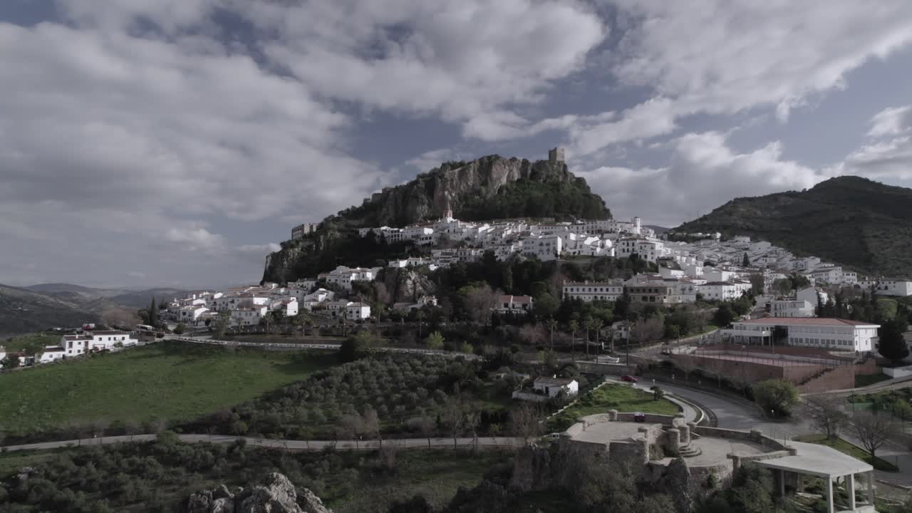 Low-altitude frontal 4K drone shot of Zahara de la Sierra, Spain, filmed with a DJI at 30fps. A cinematic view of the charming village with its historic castle in the background.