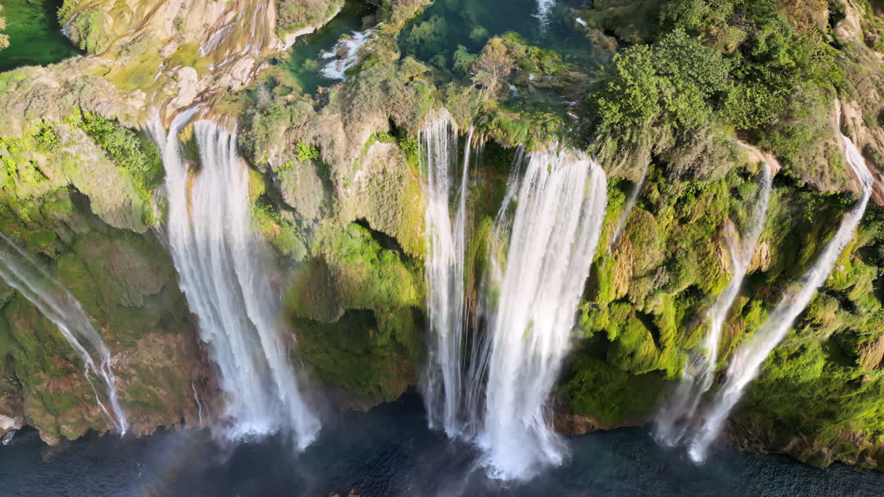 Aerial drone view of Tamul Waterfall cascading down green cliffs into a turquoise pool below