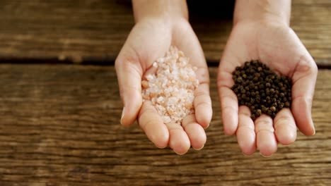 Hands-holding-sea-salt-and-black-pepper-against-wooden-table-4k