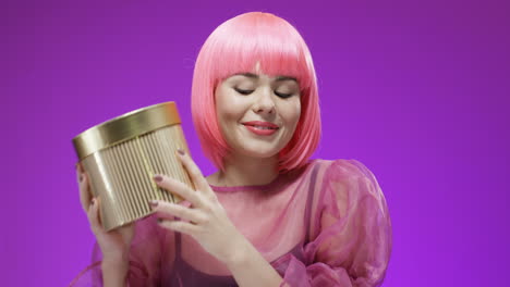 bella mujer con una peluca rosa sosteniendo una caja dorada con un regalo y sonriendo