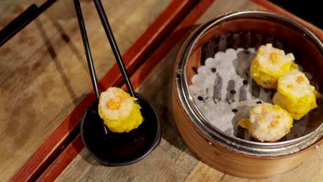 chopsticks picking dumplings from a bamboo steamer