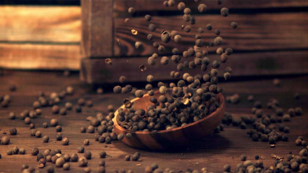 Grani di pimento che cadono in una ciotola di legno al rallentatore.