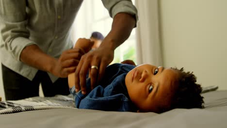 Mid-section-of-black-father-helping-his-son-changing-his-clothes-on-bed-in-a-comfortable-home-4k