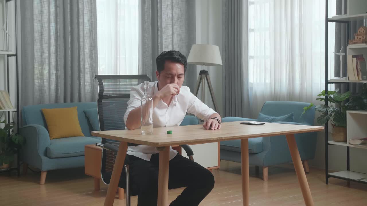 술에 취한 아시아인 남자가 테이블 위에 스마트폰을 들고 보드카를 마시며 집에서 잠을 자고 있다.