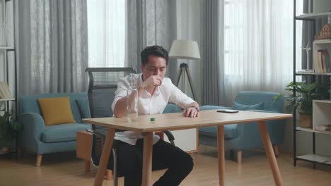 술에 취한 아시아인 남자가 테이블 위에 스마트폰을 들고 보드카를 마시며 집에서 잠을 자고 있다.