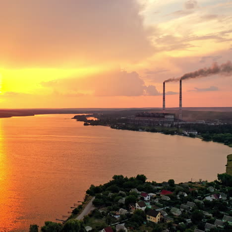 aerial landscape with sunset view over the river. beautiful evening river with sun reflection. two big pipes with smoke from the power plant near the water. camera moves right.
