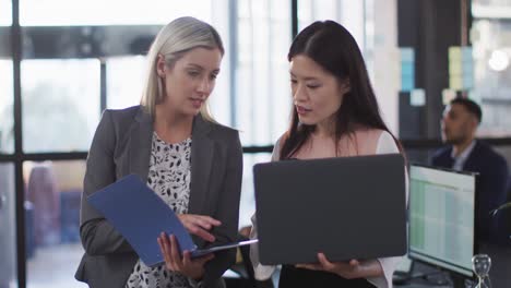 dos mujeres de negocios diversas discutiendo juntas y usando una computadora portátil en la mesa