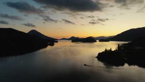 aerial view of small boat traveling through golden sunlight and silhouetted peninsulas in elaine bay in pelorus sound te hoiere of marlborough sounds, south island of new zealand aotearoa