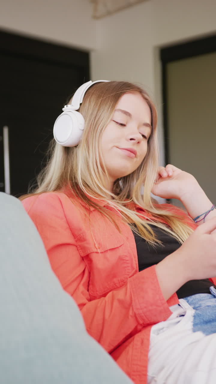 Vertical video of happy caucasian teenager girl wearing headphones, slow motion