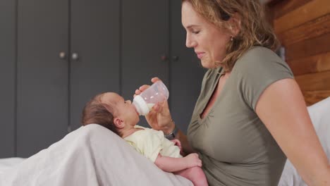 Video-Einer-Glücklichen-Kaukasischen-Mutter,-Die-Ihr-Neugeborenes-Baby-Mit-Der-Flasche-Auf-Dem-Bett-Füttert