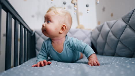 tiny blue-eyed caucasian infant in his crib. adorable baby boy trying to look above the handrail of a cot.