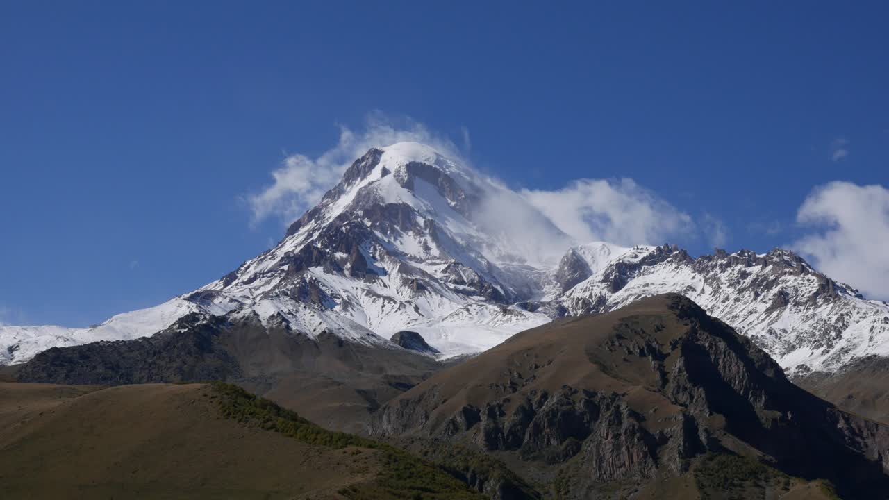 el monte kazbek o kazbegi está cubierto de nieve. el viento sopla nieve desde la cima de la montaña. stepantsminda, georgia