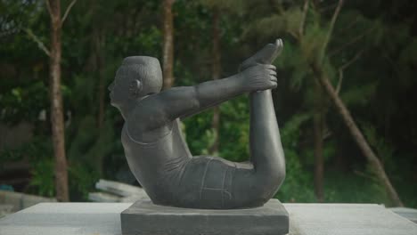 estatua de un hombre sosteniendo sus pies en la postura de yoga dhanurasana