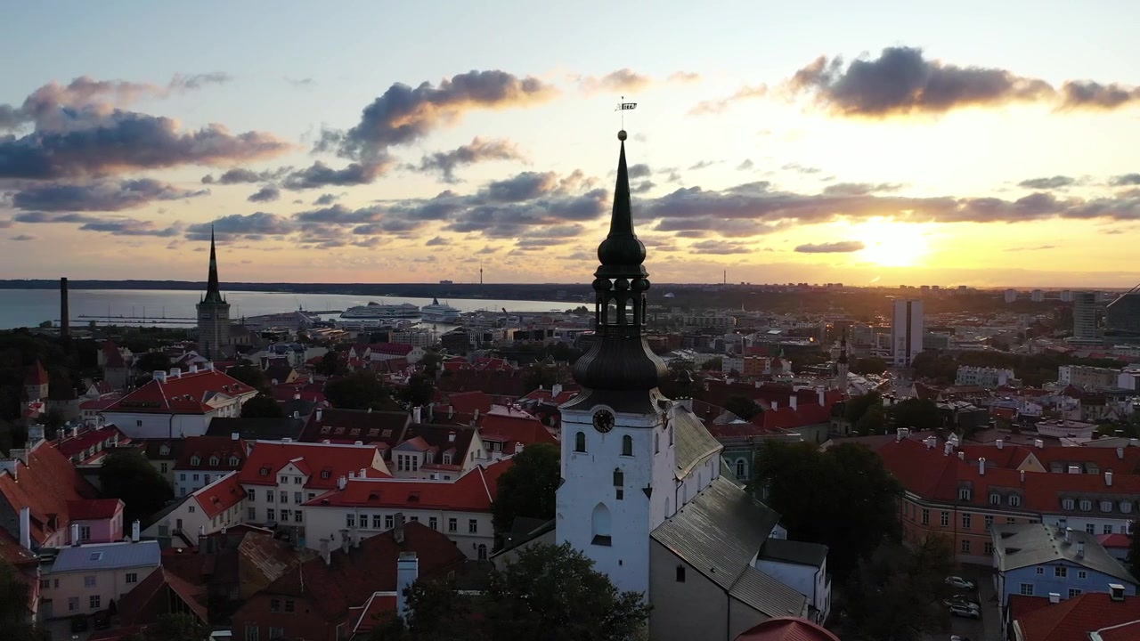 Impresionantes imágenes de dron del casco antiguo medieval de Tallin al atardecer. La toma muestra la colina de Toompea, la Catedral de Santa María y edificios con tejados rojos bajo un cielo dramático de nubes rosas y naranjas.