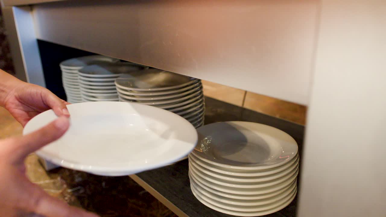 Un primo piano mostra una mano che prende diversi piatti di ceramica bianchi da una pila.