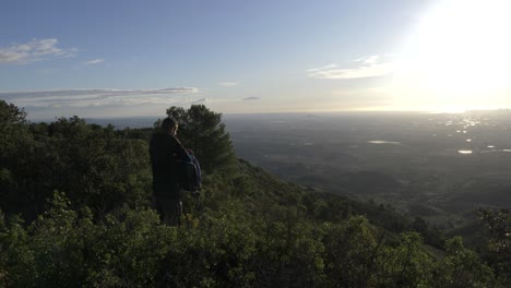 man on top of a mountain looking for sunglasses in his rucksack while looking at the sunrise