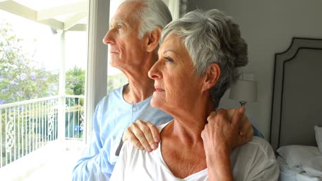 Senior-couple-looking-through-window-in-bedroom