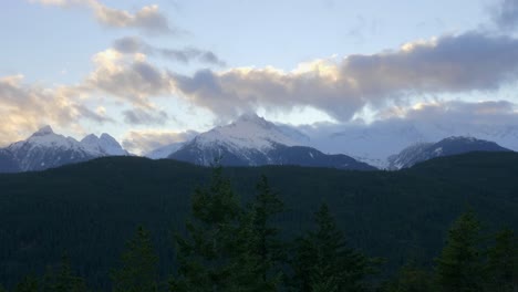 forested mountains with snowcapped summits in background