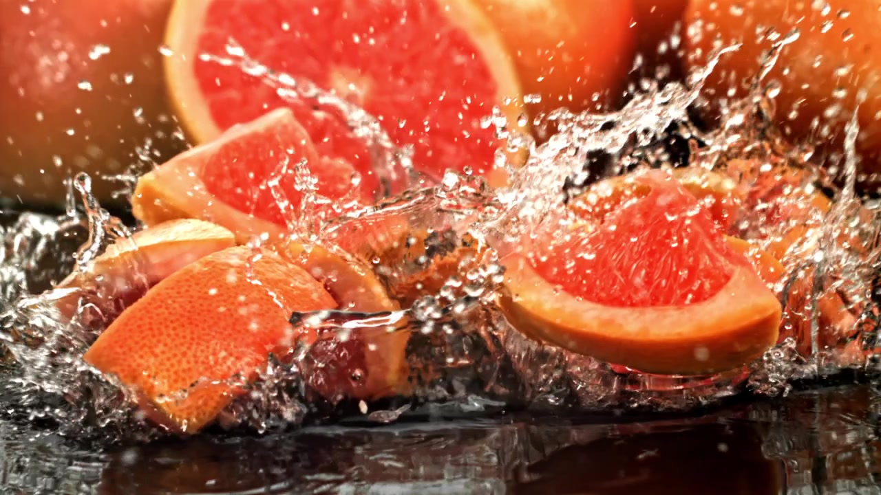 Røde grapefruktskiver som faller ned i vann i sakte film