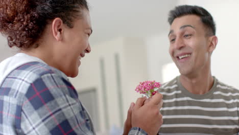 romantic diverse gay male couple giving flower and embracing in living room, slow motion