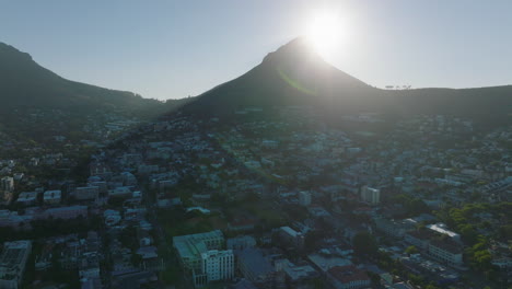 Forwards-fly-above-residential-buildings-in-suburbs.-Lions-Head-mountain-against-sun.-Cape-Town,-South-Africa