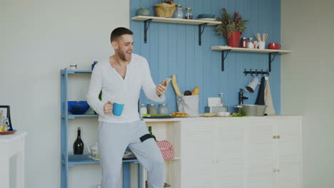 man using smartphone in kitchen while drinking coffee