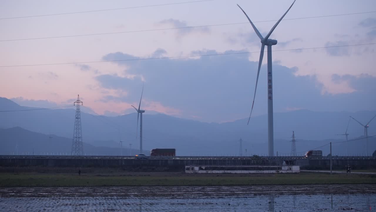 A large Chinese windfarm located in the valley of Sichuan located in between traditional chinese farms during sunset