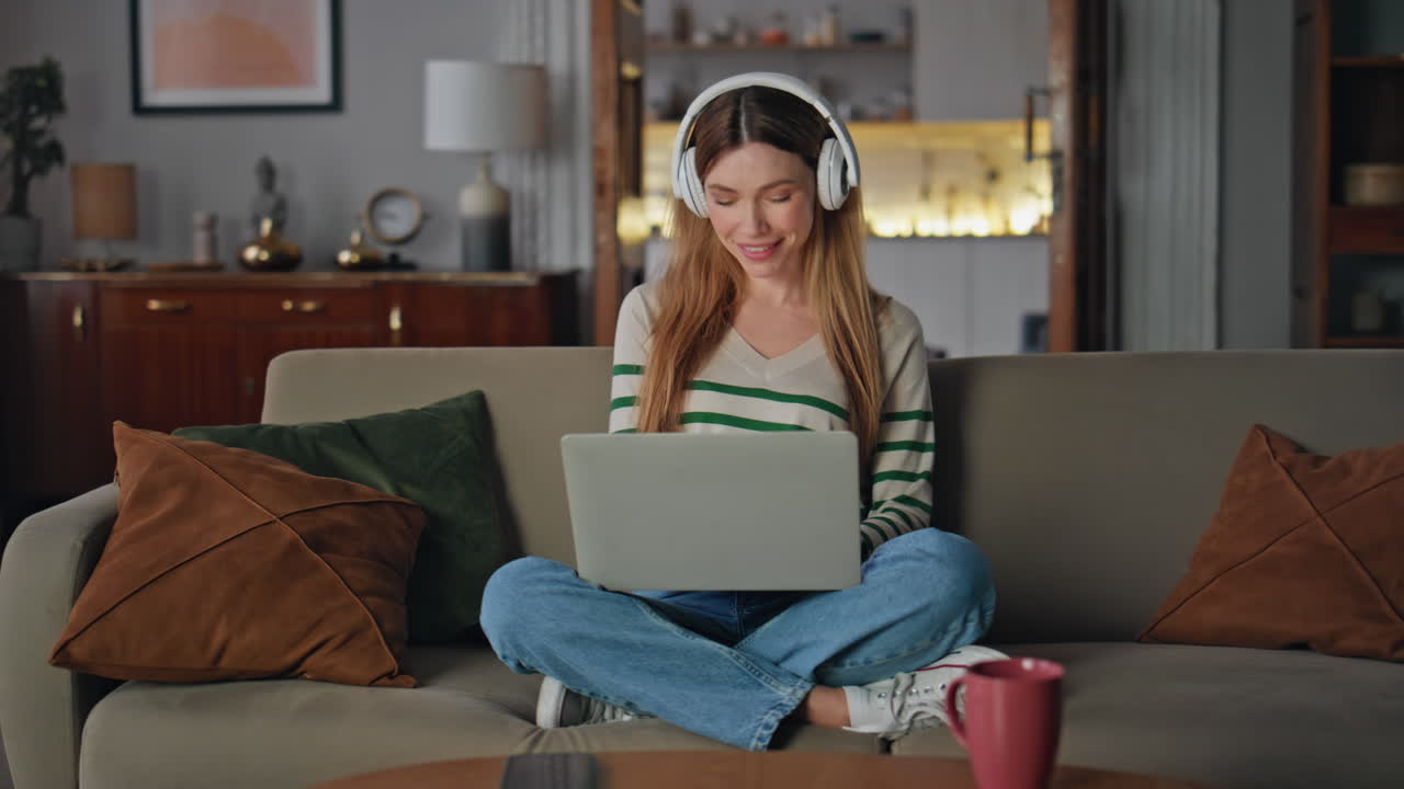 Happy freelancer listening music in wireless earphones working laptop on sofa.