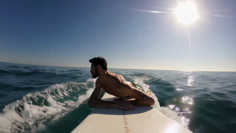 a man paddling on a surfboard in the ocean under a bright sun