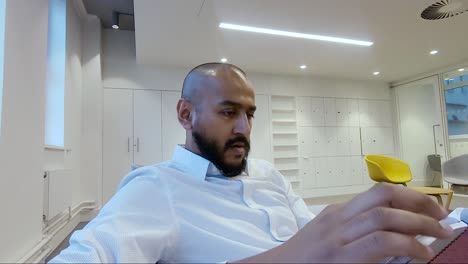 Asian-Indian-Male-sitting-down-in-office-reading-a-notepad