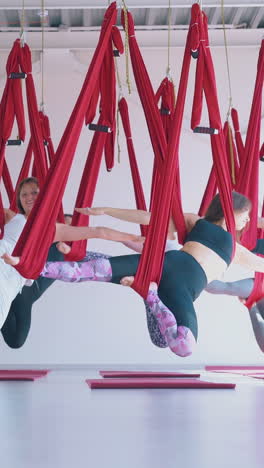 concentrated strong women team hangs in special red fly yoga hammocks in warrior asana with open arms