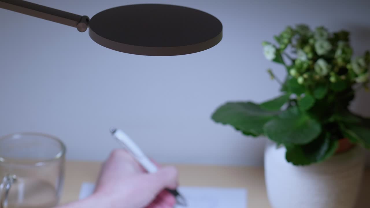 imágenes de zoom-out de una lámpara de escritorio de pie sobre la mano humana que está dibujando bocetos en papel en una mesa de trabajo