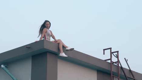 pretty-tanned-lady-with-dark-loose-hair-sits-on-roof