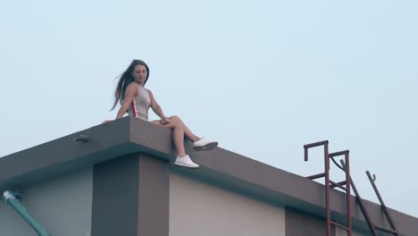 pretty tanned lady with dark loose hair sits on roof