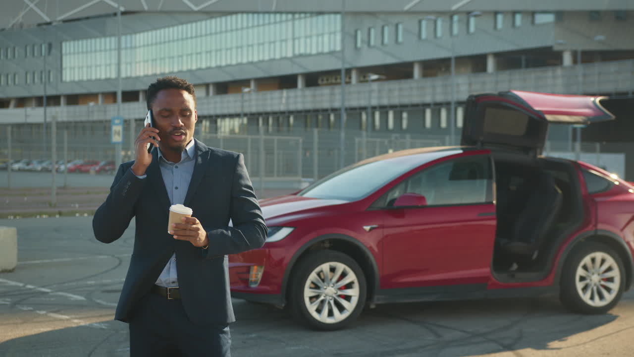 hombre de negocios hablando por teléfono cerca de un coche eléctrico en el estacionamiento